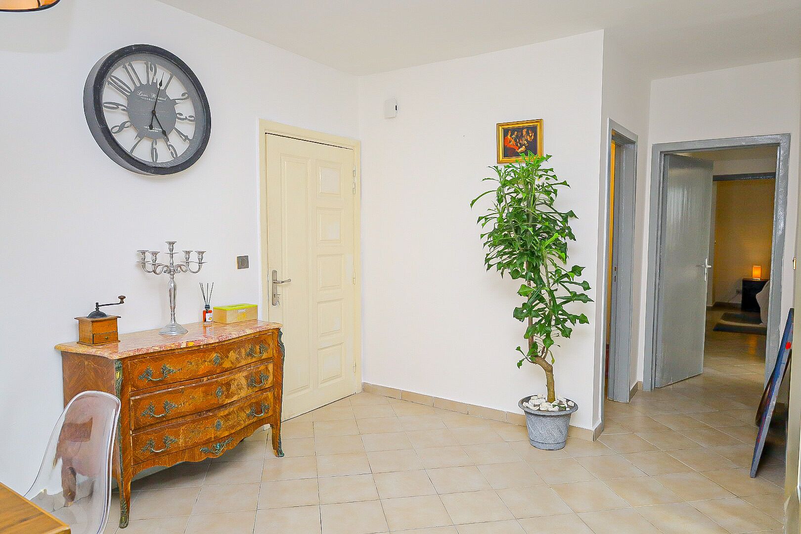 Um quarto com cômoda de madeira, uma planta em vaso, um relógio de parede e uma porta.