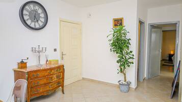 Um quarto com cômoda de madeira, uma planta em vaso, um relógio de parede e uma porta.