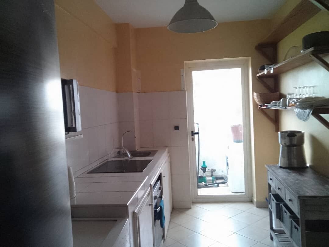 Une cuisine équipée d’un évier, d’une cuisinière et de placards. Une porte donne accès à un espace extérieur.
