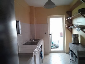 A kitchen with a sink, stove, and cabinets. There is a door leading to an outdoor area.