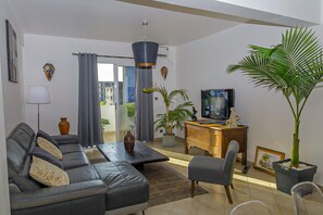 Una sala de estar con un sofá, una mesa de centro, un televisor, un escritorio y una planta en maceta.