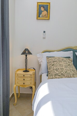Un dormitorio con una cama, una mesita de noche con lámpara, un teléfono en la pared y un cuadro enmarcado.