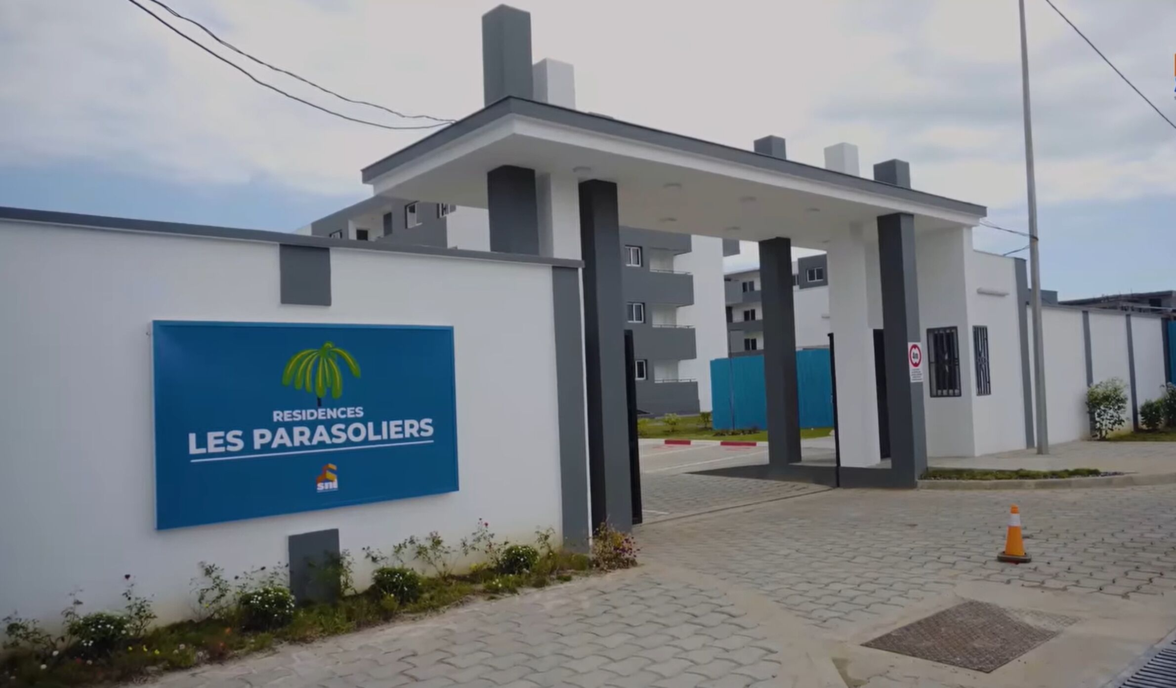 Un bâtiment moderne, sur lequel on peut lire l’inscription « RÉSIDENCES LES PARASOLIERS », et dont l’entrée est protégée par un portail.