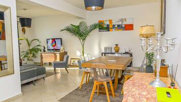 A modern living room with a dining area, a television, and a large plant.