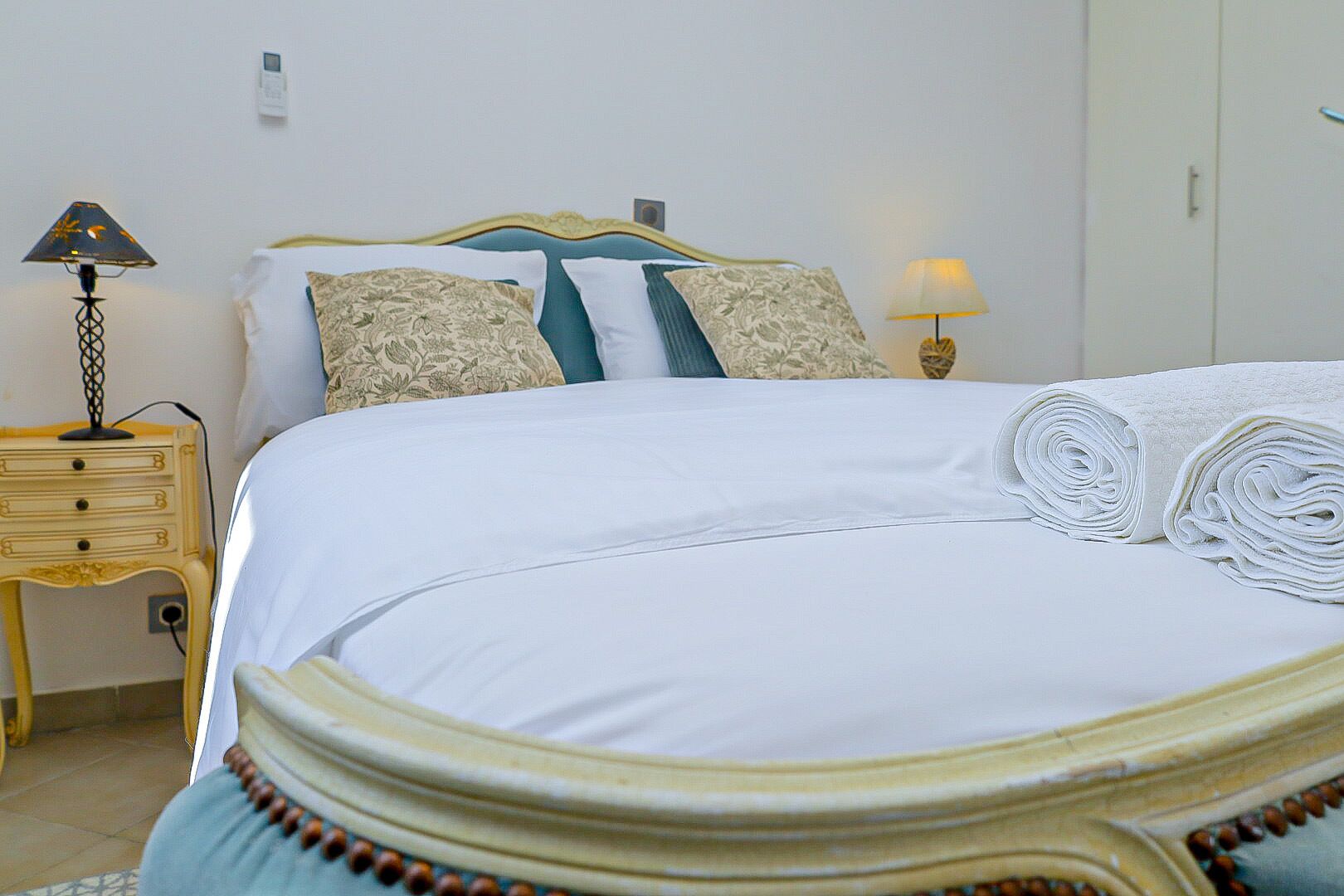 A neatly made bed with a white duvet, a rolled white towel, and a decorative headboard.