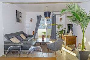 A living room with a sofa, chairs, a coffee table, a TV, and a potted plant.