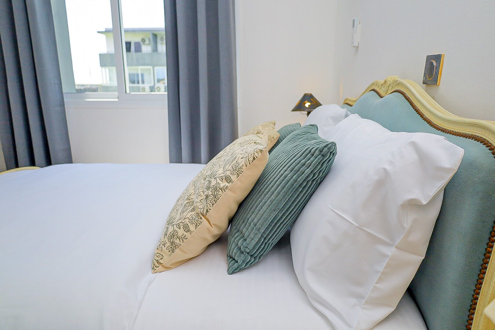 A bed with a white sheet, a beige pillow with a floral pattern, and two green pillows.