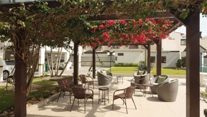 Ein Außenbereich mit Korbmöbeln unter einer Pergola mit blühenden Weinreben.
