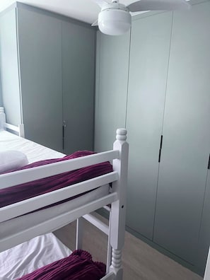 Ein Etagenbett mit weißem Kopfteil, einem Deckenventilator und grauen Schrankelementen.