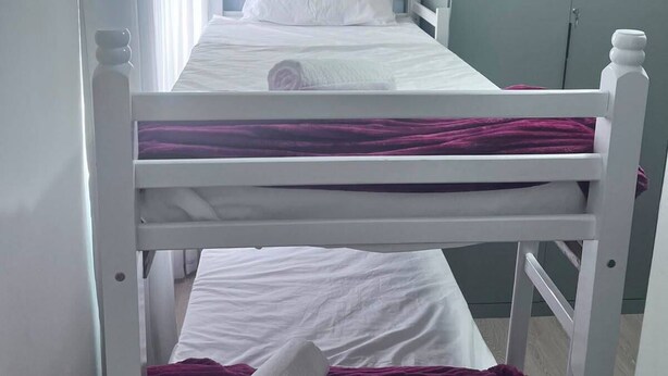 Ein Etagenbett mit weißer Bettwäsche und einer violetten Decke, ein Kleiderschrank und ein Vorhang.