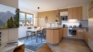 A modern kitchen with wooden cabinets, a built-in oven, and a dining area with a table and chairs. - Horngacher Top 1 App (Kirchberg in Tirol)