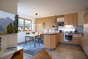 A modern kitchen with wooden cabinets, a built-in oven, and a dining area with a table and chairs. - Horngacher Top 1 App (Kirchberg in Tirol)