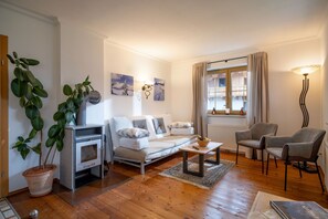 A modern living room with a sofa, a coffee table, a fireplace, a window with curtains, and a plant. - Horngacher Top 1 App (Kirchberg in Tirol)