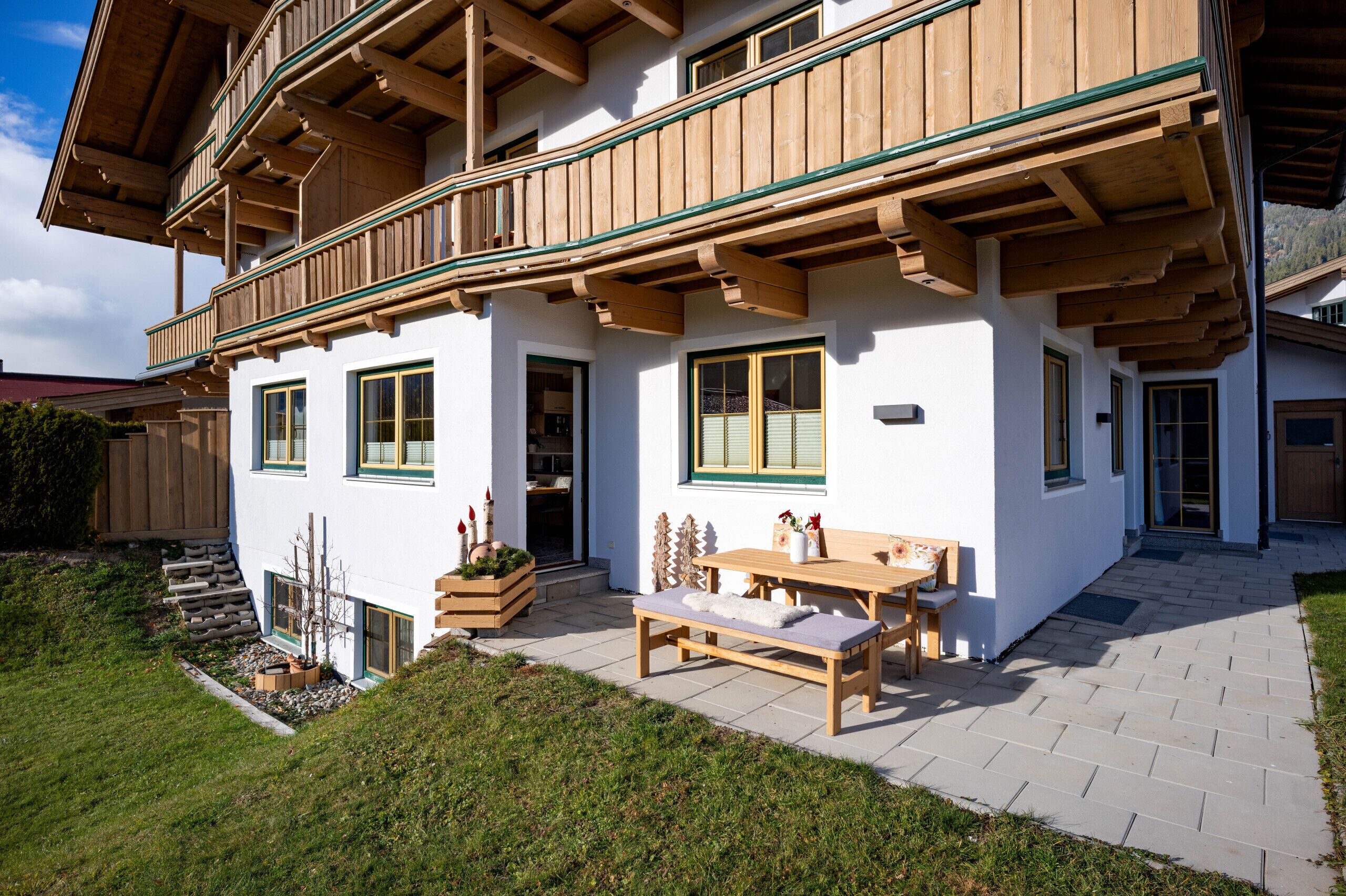 A two-story building with a balcony, wooden beams, and a patio area with a table and benches.
