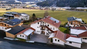 A residential area with houses featuring sloped roofs and solar panels, surrounded by snow-covered mountains and a clear sky. - Horngacher Top 1 App (Kirchberg in Tirol)
