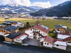 A residential area with houses featuring sloped roofs and solar panels, surrounded by snow-covered mountains and a clear sky. - Horngacher Top 1 App (Kirchberg in Tirol)