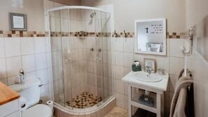 A bathroom with a toilet, shower, sink, and towel rack. - Dassenheuwel Farm Cottages (Malmesbury)