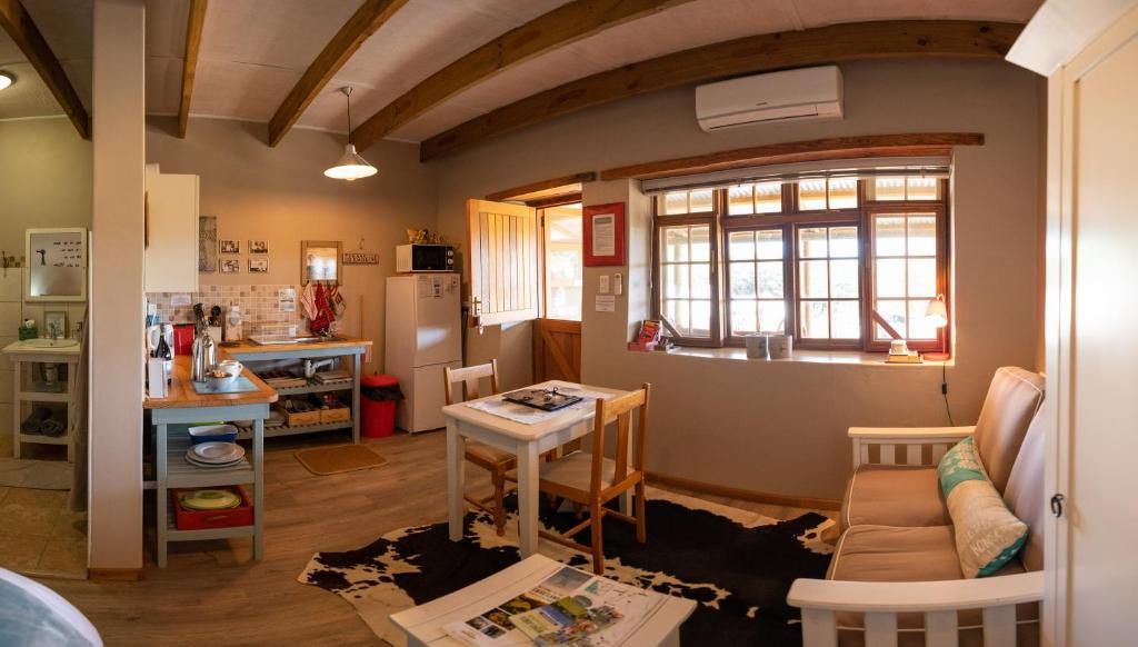 A cozy living room with a wooden ceiling, a dining area with a table and chairs, a sofa, and a window with blinds.