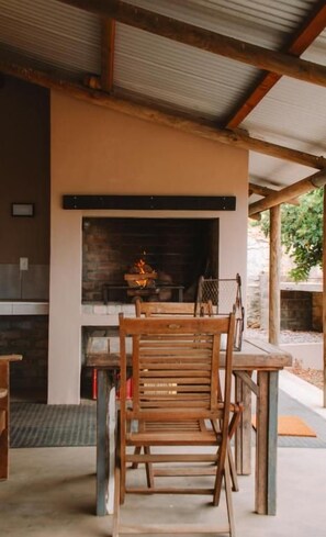 An outdoor seating area with a built-in fireplace, wooden chairs, and a table. - Dassenheuwel Farm Cottages (Malmesbury)