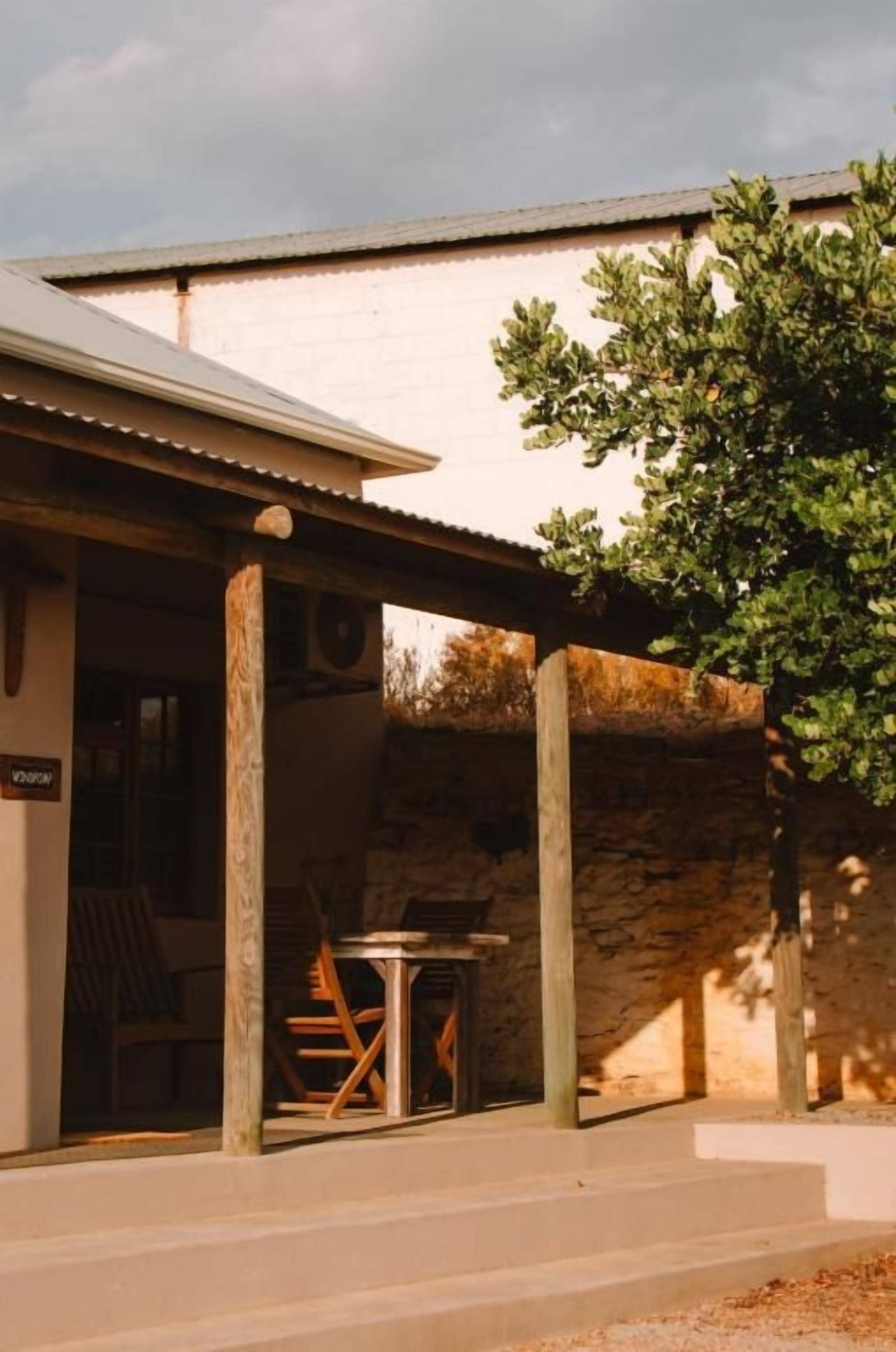 Un edificio con un espacio de estar al aire libre cubierto, un muro de piedra y un árbol.