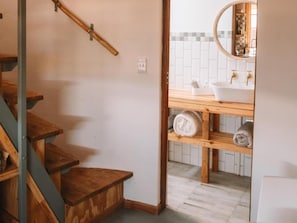 A wooden staircase leading to a bathroom with a white sink and a mirror. - Dassenheuwel Farm Cottages (Malmesbury)