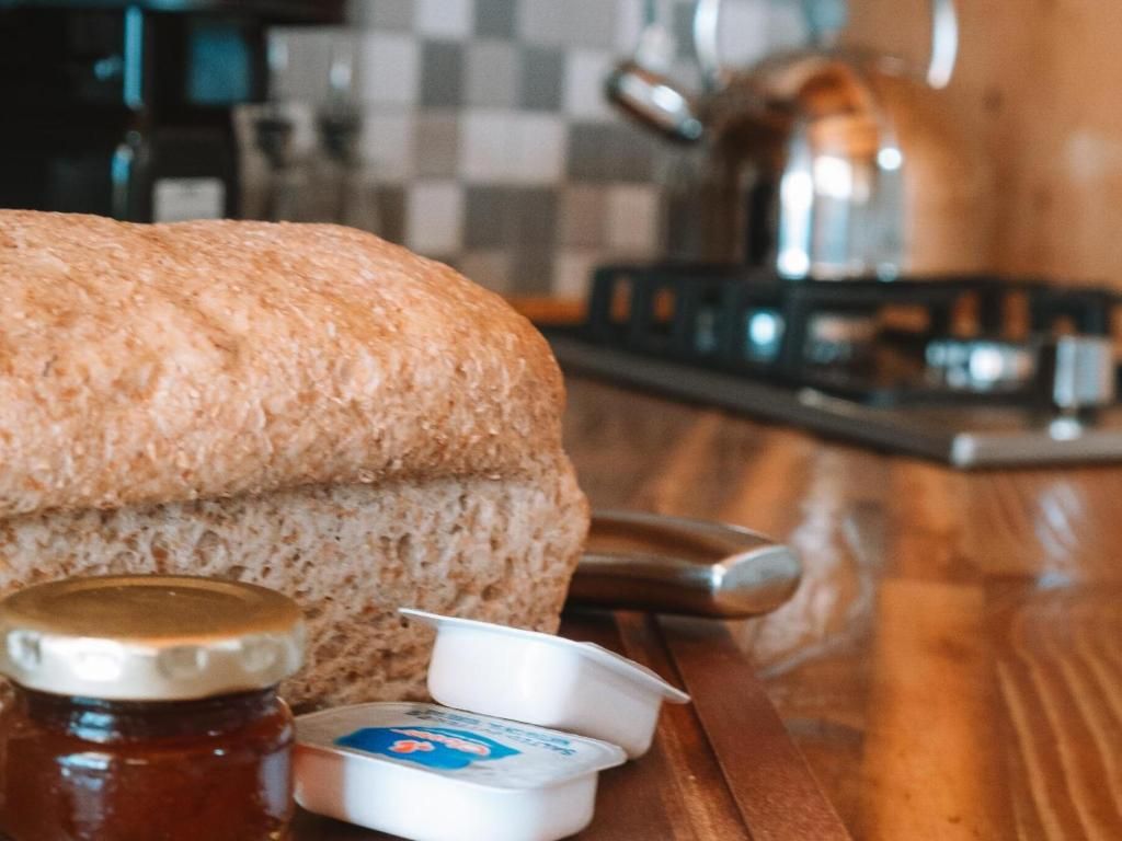 A loaf of bread, a jar of jam, and a container of butter on a wooden surface.