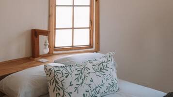 A bedroom with a bed, pillows, a nightstand, and a window.