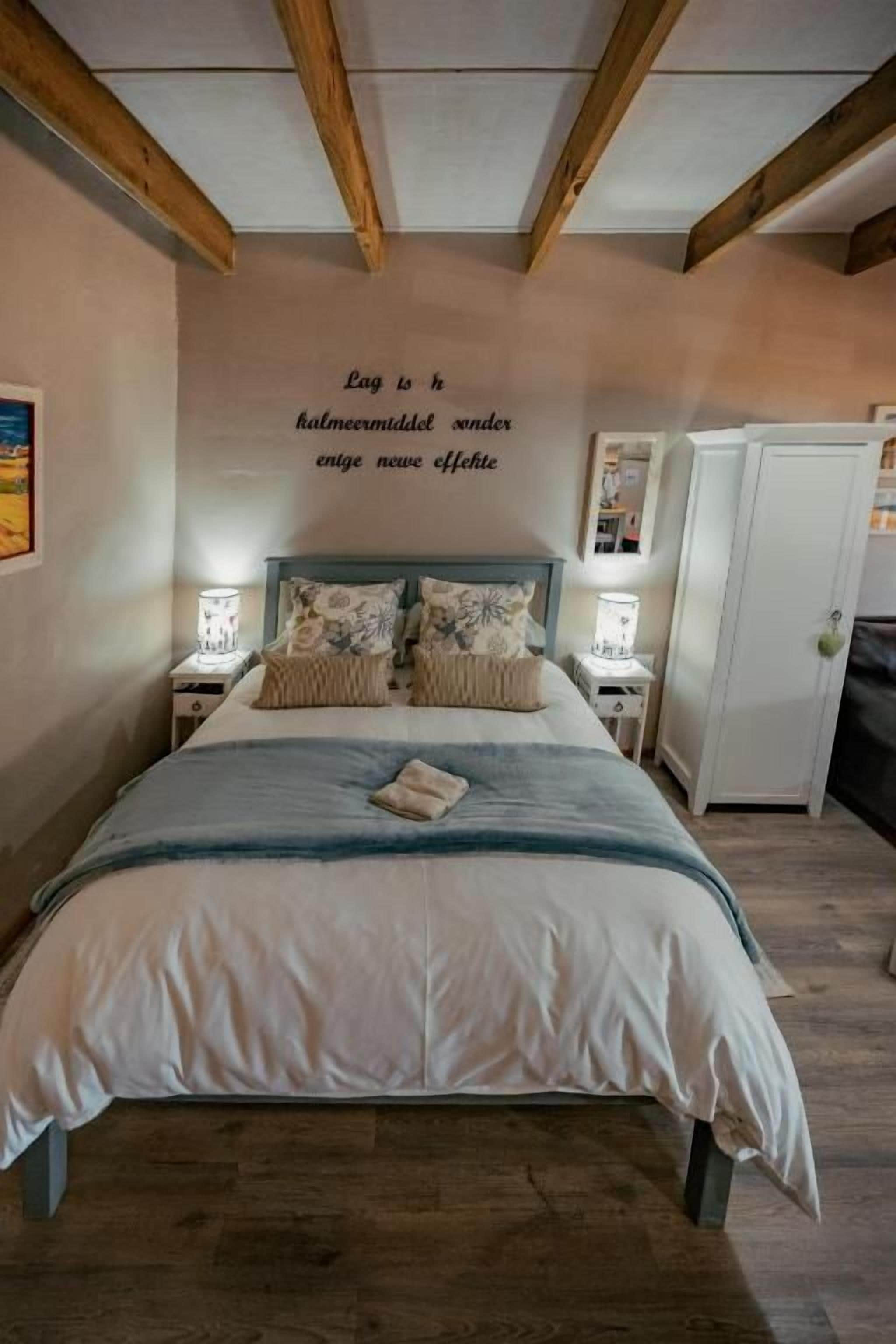 A bedroom with a bed, bedside tables, a wardrobe, and a wall with a motivational quote.