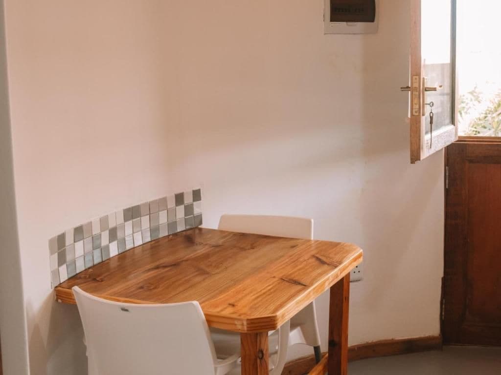 A room with a wooden dining table and white chairs, a tiled backsplash, and a wooden door.