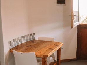 Een kamer met een houten eettafel en witte stoelen, een betegelde achterwand en een houten deur.