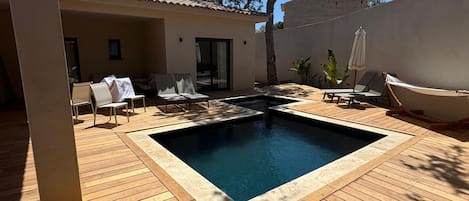 A wooden deck with a swimming pool, lounge chairs, and a covered seating area.