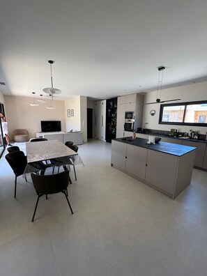 A modern kitchen with a central island, dining area with chairs, and a TV. - Contemporary 4-bedroom villa—with pool and hot tub—7 minutes from Pinarello (Zonza)