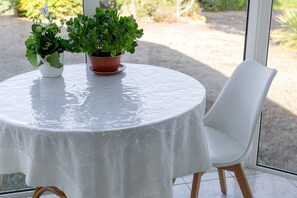 Una mesa redonda con mantel blanco, dos plantas en macetas y una silla blanca.
