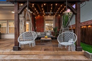 A covered patio area with two white swing chairs, a gray sofa, and a small table with fruit.