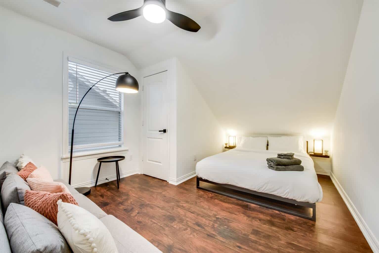 A bedroom with a bed, bedside lamps, a ceiling fan, and a window with blinds.