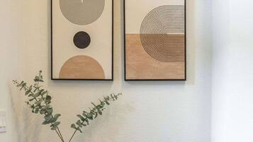 A black console table with a 'welcome' sign, two framed abstract artworks, and a vase with green foliage.