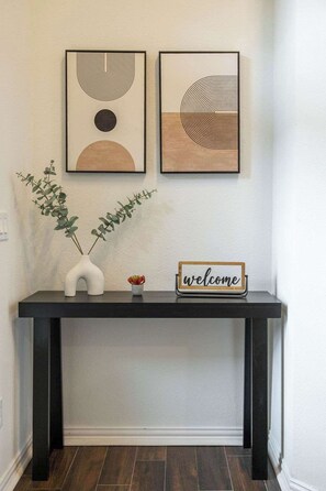 A black console table with a 'welcome' sign, two framed abstract artworks, and a vase with green foliage. - Poolside Paradise | Hot Tub & Patio (5-BD/2.5BA) (Princeton)