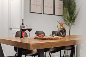 A dining table with a bottle of red wine, two glasses, a fruit platter, and a decorative vase.