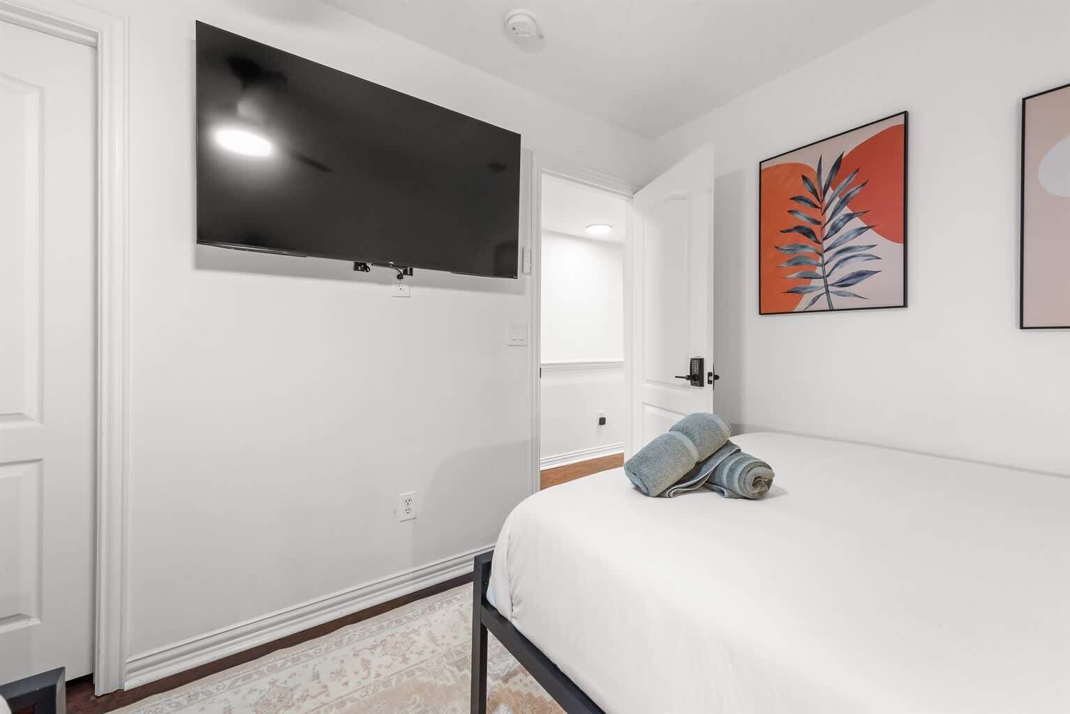 A hotel room with a bed, a flat-screen TV mounted on the wall, and a door leading to another room.