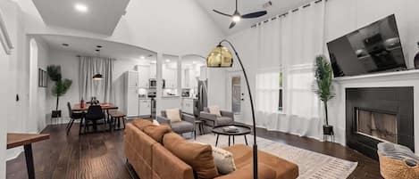 A modern living room with a sofa, a dining area, and a kitchen in the background.