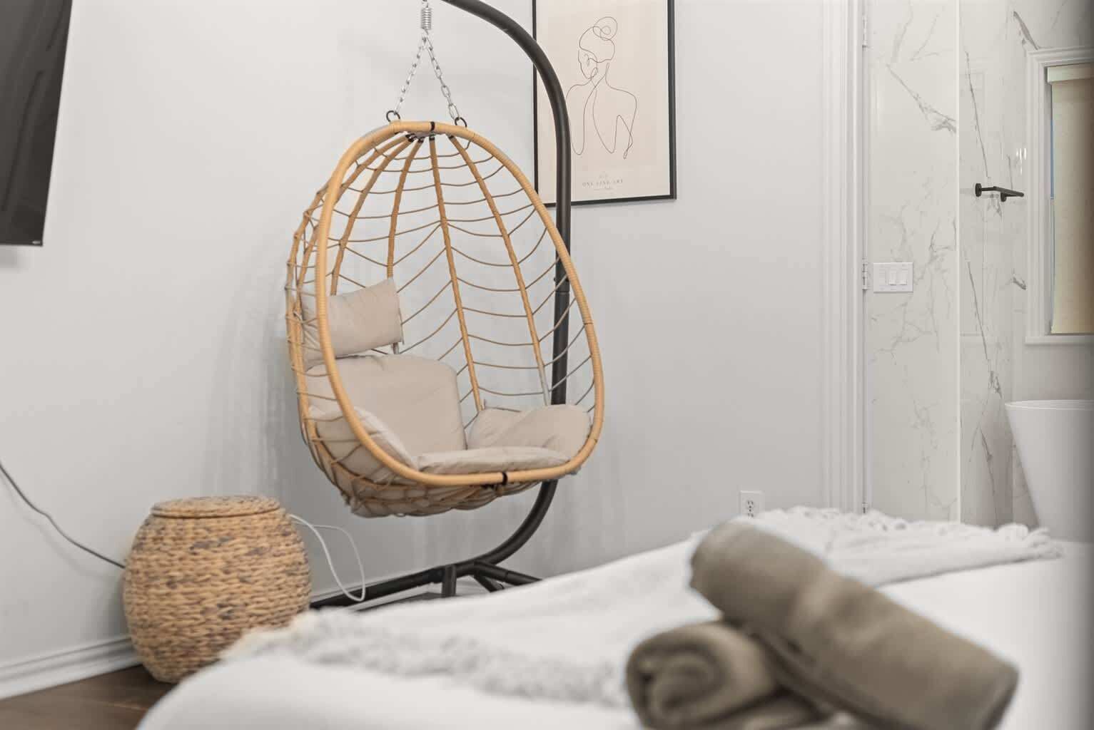 A room with a hanging chair, a woven basket, and a bed with rolled towels.