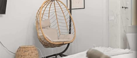 A room with a hanging chair, a woven basket, and a bed with rolled towels.