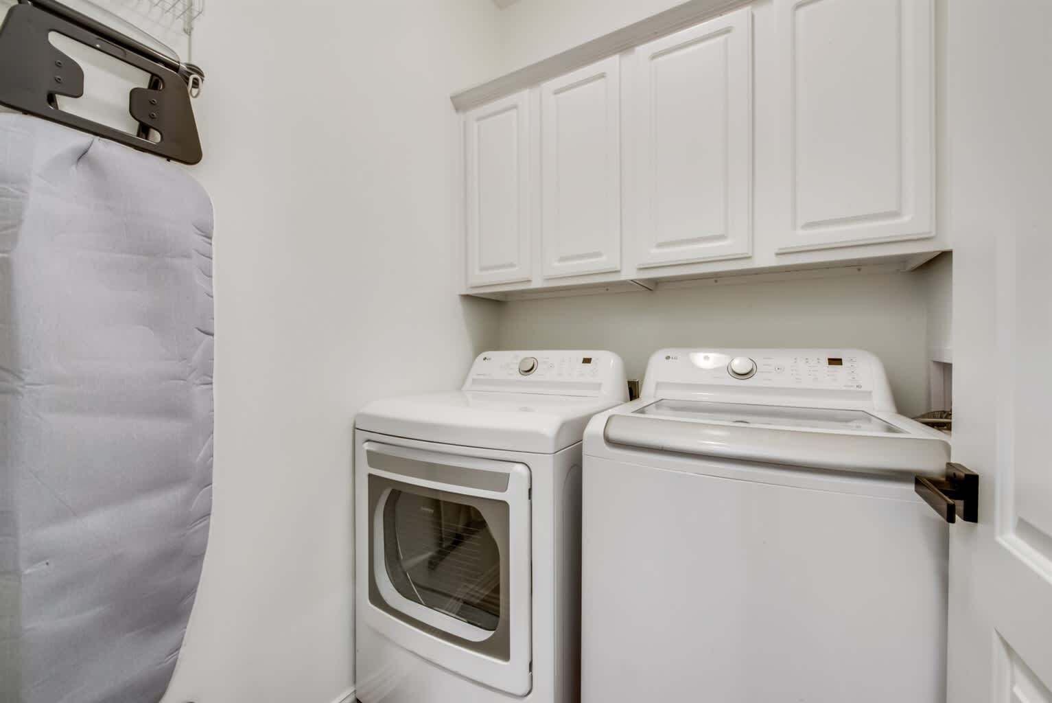 A laundry room with two white washing machines and a dryer, a white towel hanging on a rack, and white cabinets above the machines.