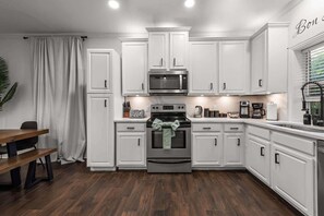 A modern kitchen with white cabinetry, a stainless steel oven, and a dining area with a wooden table and chairs.
