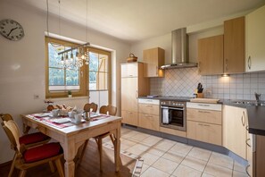 A kitchen with wooden cabinets, a built-in oven, and a dining area with a table set for breakfast. - Horngacher Top 2 App (Kirchberg in Tirol)