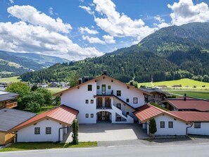 A large white building with multiple floors and a red roof, surrounded by lush green hills and a clear blue sky. - Horngacher Top 2 App (Kirchberg in Tirol)