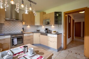 A modern kitchen with wooden cabinets, a built-in oven, a coffee maker, and a dining area with a table set for two. - Horngacher Top 2 App (Kirchberg in Tirol)