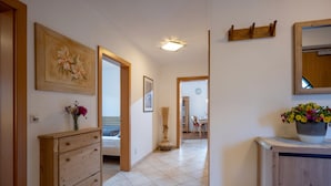 A hallway with a wooden dresser, a painting, a vase with flowers, and a potted plant. - Horngacher Top 2 App (Kirchberg in Tirol)