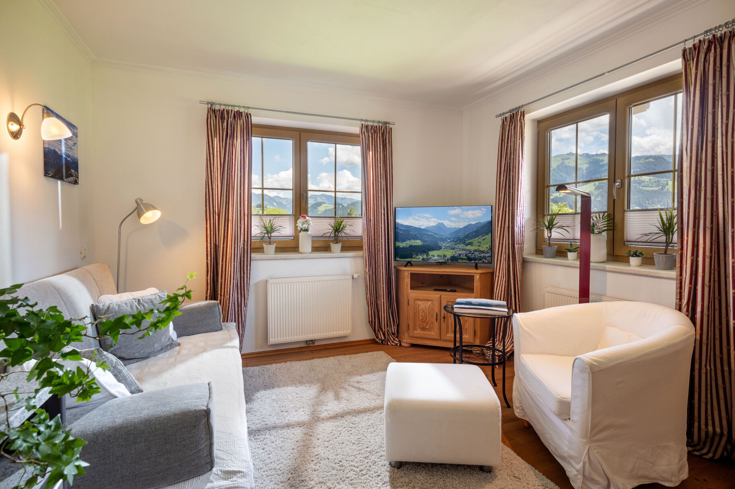 A living room with a sofa, a white armchair, a TV, and a radiator.