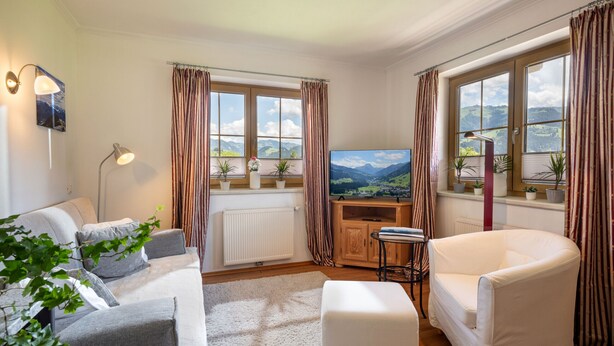 A living room with a sofa, a white armchair, a TV, and a radiator. - Horngacher Top 2 App (Kirchberg in Tirol)